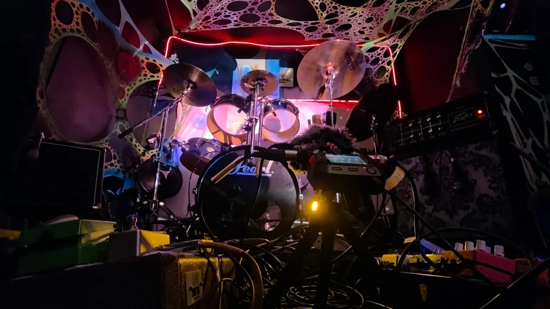 Palco com bateria, pedais e luz neon rosa e azul